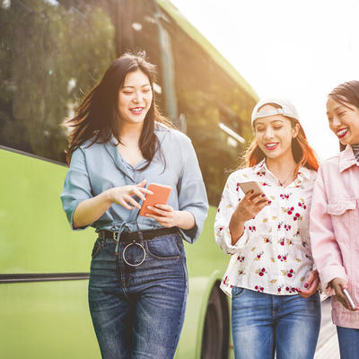 Three young women walking while talking to each other with confort costume holding phones and drinks.